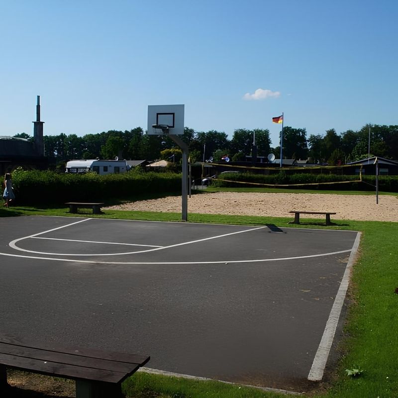 Ein Basketballplatz mit einem Netz und einer Bank und dahinter ein Strandvolleyballfeld.