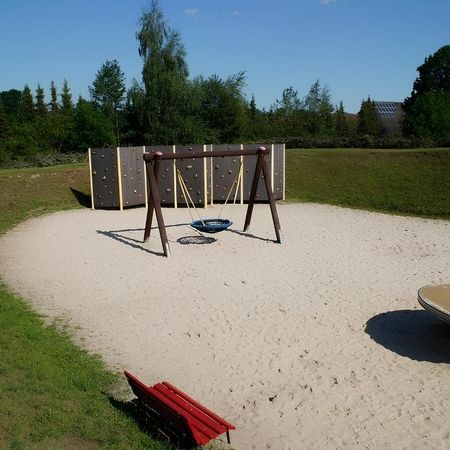 Ein Spielplatz mit einer Schaukel, Kletterwand und einer Bank, ideal für Kinder und Eltern zum Entspannen und Spielen.