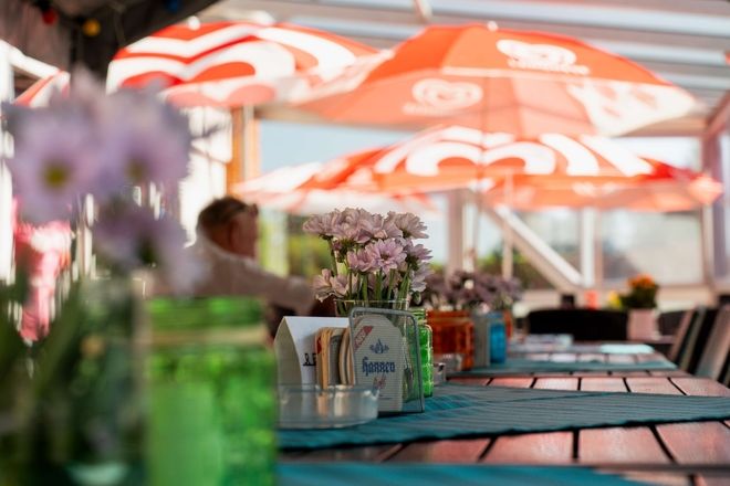 Blumengeschmückte Sitzplätze auf der Terrasse am Kiosk Rotbuche mit bunten Windlichtern und türkisfarbenen Tischläufern unter roten Sonnenschirmen