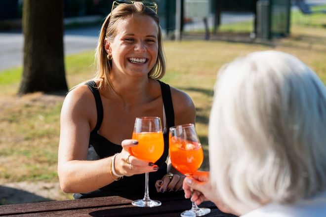 Eine Frau hebt ein Glas Orangensaft zum Anstoßen und strahlt Freude aus